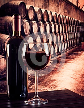 Red wine glass near bottle in old wine cellar background