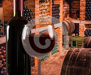 Red wine glass near bottle on old wine cellar background with space for text