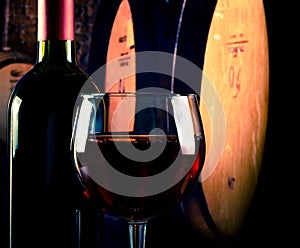 Red wine glass near bottle on old wine cellar background with space for text