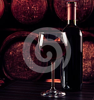 Red wine glass near bottle on wood table and in old wine cellar background