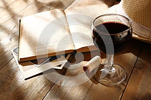 Red wine glass and old book on wooden table at sunset burst. vintage filtered image