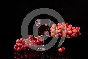 Red wine in a glass and pink grapes on a black background