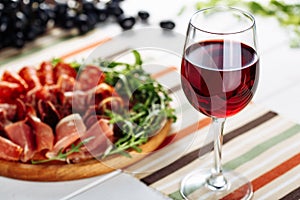 Red wine glass with sliced jamon plate on table background. Horizontal close-up view