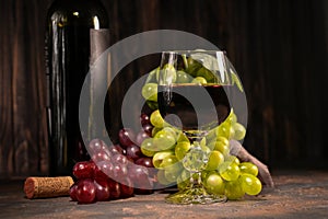 Red wine in glass with vintage bottle and with bunch of red and white grapes on wooden background