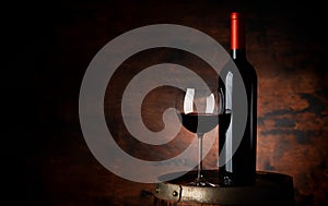 Red wine glass and wine bottle on old wooden barrel