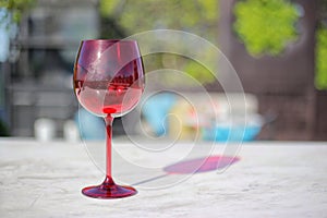 Red wine glasses liquor cocktails reflecting blue sky with a few clouds on marble table with blur colorful sofa in background. Con