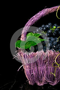 Red wine grapes in voiolet basket on bllack background.