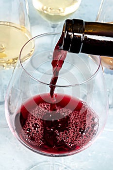 Red wine pour in a large glass at a tasting, with more glasses of wine