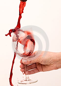 Red wine is poured into a glass held by a hand