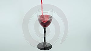 Red wine poured into goblet decorated with heart on white background.