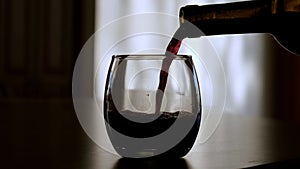 Red Wine poured into a stemless glass in dark room, backlit.