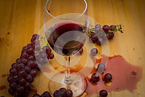 Red wine poured into wine glass and spilled on wooden table with fresh grapes as background design