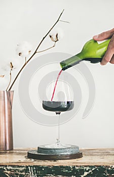 Red wine pouring from bottle in man`s hand into wineglass