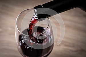 Red wine pouring from the bottle to the wine glass above, close up view on a wooden table