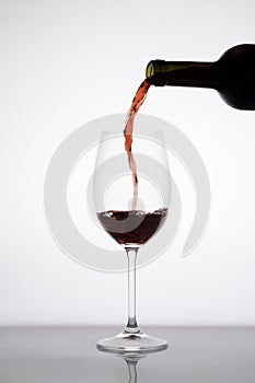 Red wine pouring into a glass from bottle isolated on white background