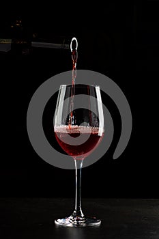 Red wine pouring into a glass with drops on black background