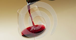 Red wine pouring into glass over yellow background with copy space