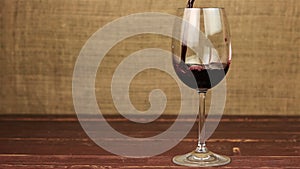 Red wine pouring into glass on wooden table