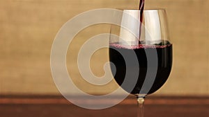 Red wine pouring into glass on wooden table