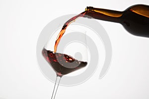 Red wine pouring into tilted wineglass from bottle.