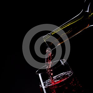 Red wine pouring into wine glass isolated on black