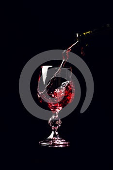 Red wine pouring into wine glass with splash, isolated on black