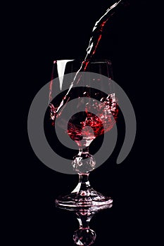 Red wine pouring into wine glass with splash, isolated on black