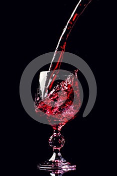 Red wine pouring into wine glass with splash, isolated on black