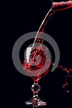 Red wine pouring into wine glass with splash, isolated on black