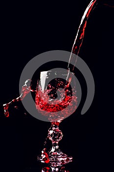 Red wine pouring into wine glass with splash, isolated on black