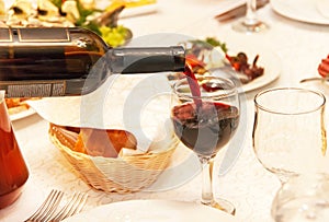 Red wine pouring into a wine glass, that standing on the table.