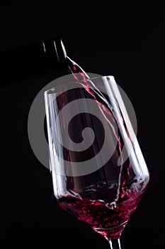 Red wine pouring in wineglass from a bottle on black background. Wine list design menu with copyspace.