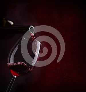 Red wine pouring in wineglass from bottle over dark background