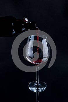 Red wine pouring into a wineglass. Isolated on black background.