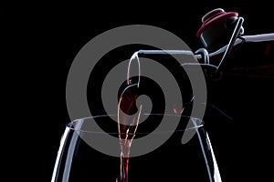 Red wine pouring into a wineglass. Isolated on black background.