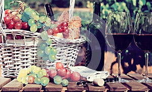 Red wine ripe grapes and picnic basket on table in vineyard