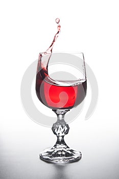 Red wine splashing in wine glass on light background