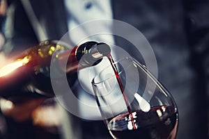 Red wine spouts into glass from bottle. Dark background