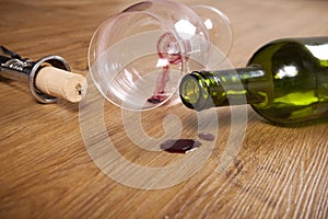 Red wine stain on wooden flooring, dirty wine glass, corkscrew, empty wine bottle