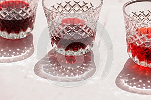 Red wine in a transparent glass with abstract shadows on pink background