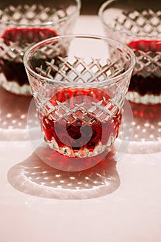 Red wine in a transparent glass with abstract shadows on pink background