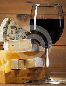 Red wine with various types of cheese on wooden background