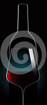 Red wine in a wine glass is seen in dramatic lighting in front of an unopened wine bottle