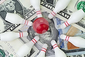 Red winning bowling strike ball surround with knocked down pins on pile of US dollar banknotes money, financial success target photo