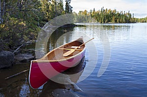 Red wood canoe on the shore of a Boundary Waters lake in morning light during autumn