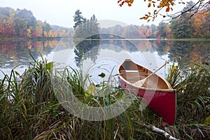 Red wood canoe on shore of a small lake with an island on a cloudy autumn morning