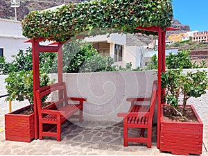 Red wooden bench on pedestrian street with flower pots in rural town. Architecture and urban furniture