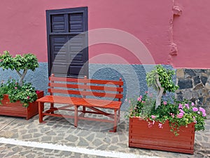 Red wooden bench on pedestrian street and stone facade with closed wooden window. Urban architecture and furniture