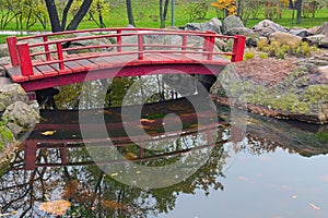 A red wooden bridge at the Japanese Garden inside the Kyoto Park in Kyiv. bridge reflected in the lake water