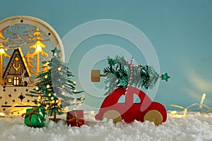 Red wooden car carrying a christmas tree over snow in front of b
